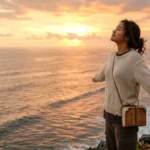 Seseorang berdiri di tepi tebing menghadap lautan saat matahari terbenam dengan ekspresi penuh harapan menggambarkan makna one day artinya suatu hari nanti